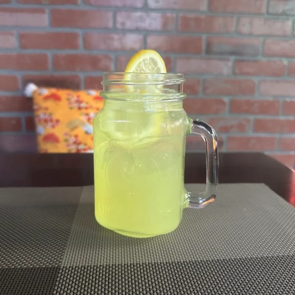 A refreshing glass of lemonade with a lemon slice, served in a mason jar on a dark placemat.
