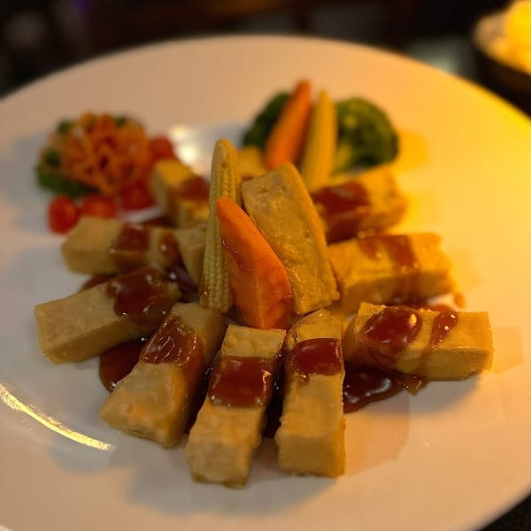 Crispy fried tofu sticks drizzled with sauce, served with baby corn, carrots, and broccoli.