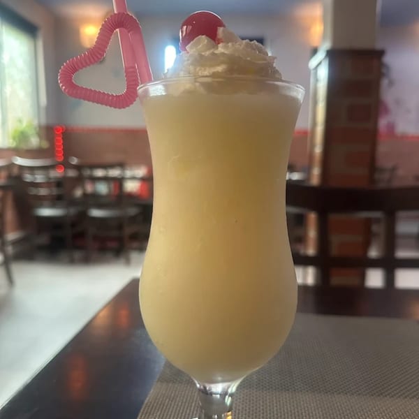 A creamy yellow drink with whipped cream, a cherry, and a heart-shaped pink straw in a restaurant.