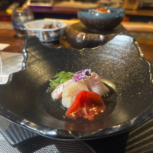 Yamashiro's sashimi dish with scallops, fish, tomato, and edible flower on a black plate.
